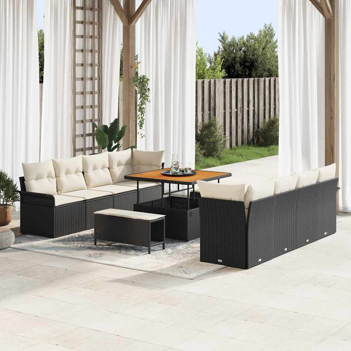 Set patio esterno con mobili in vimini neri e cuscini color crema. Include tavolo, panca e tende, con sfondo giardino.
