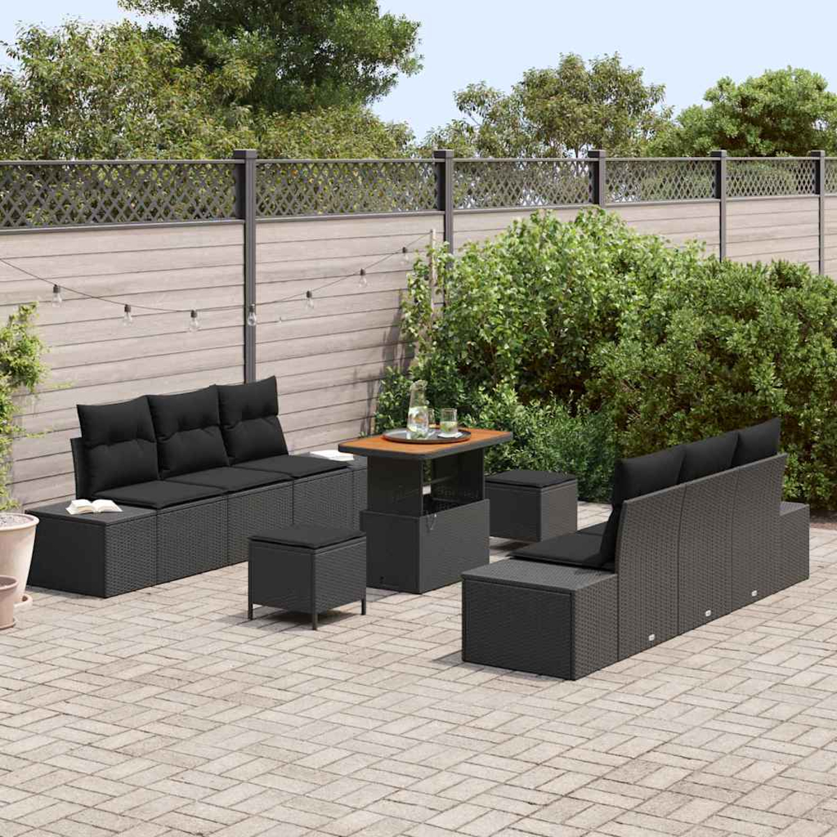 Outdoor-Terrassenset mit schwarzen Kissen. Enthält ein Sofa, einen Tisch und Hocker. Der Hintergrund zeigt einen Zaun und Grün.