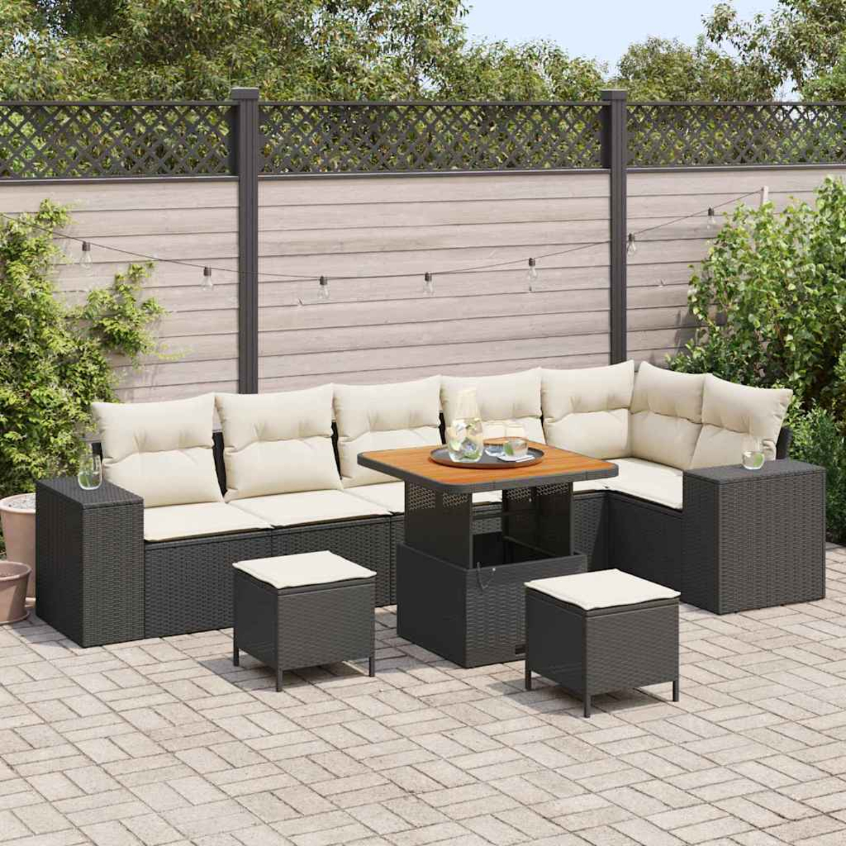 Garten-Sitzgruppe: dunkelgraues, gewebtes Sofa mit cremefarbenen Kissen, Holztisch und zwei Ottomanen auf einer Ziegelterrasse. Hintergrund: Holzzaun.