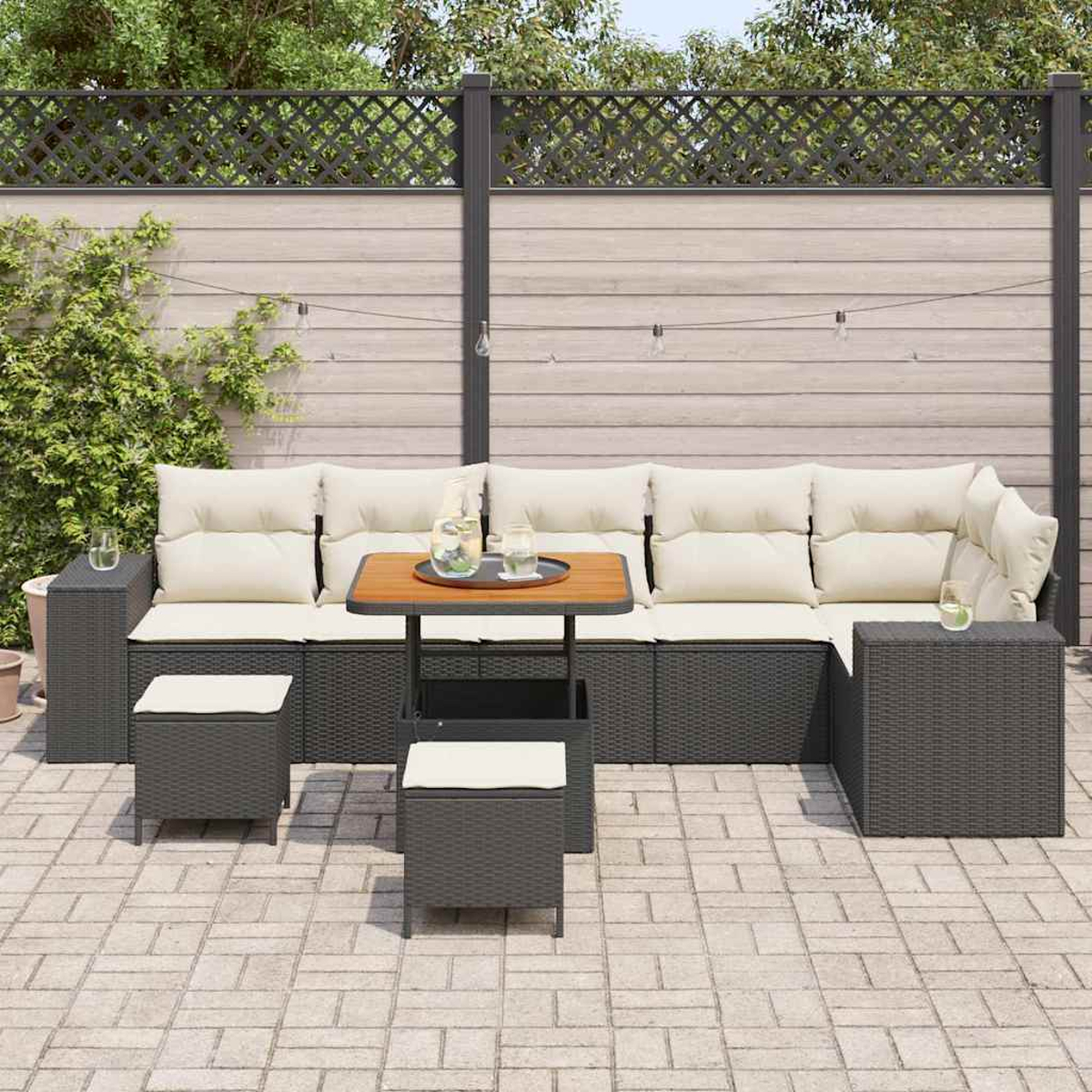 Terrassenset mit dunkelgrauen Korbmöbeln, beigefarbenen Kissen, einem kleinen Tisch mit Getränken und einem Holzzaun im Hintergrund.