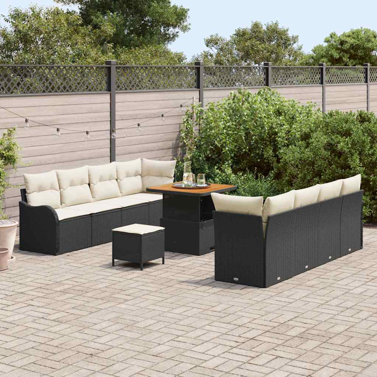 Gartenmöbel-Set. Schwarze Korbsessel mit cremefarbenen Kissen, ein Tisch und ein Hocker auf einer Ziegelstein-Terrasse, mit Zaun.