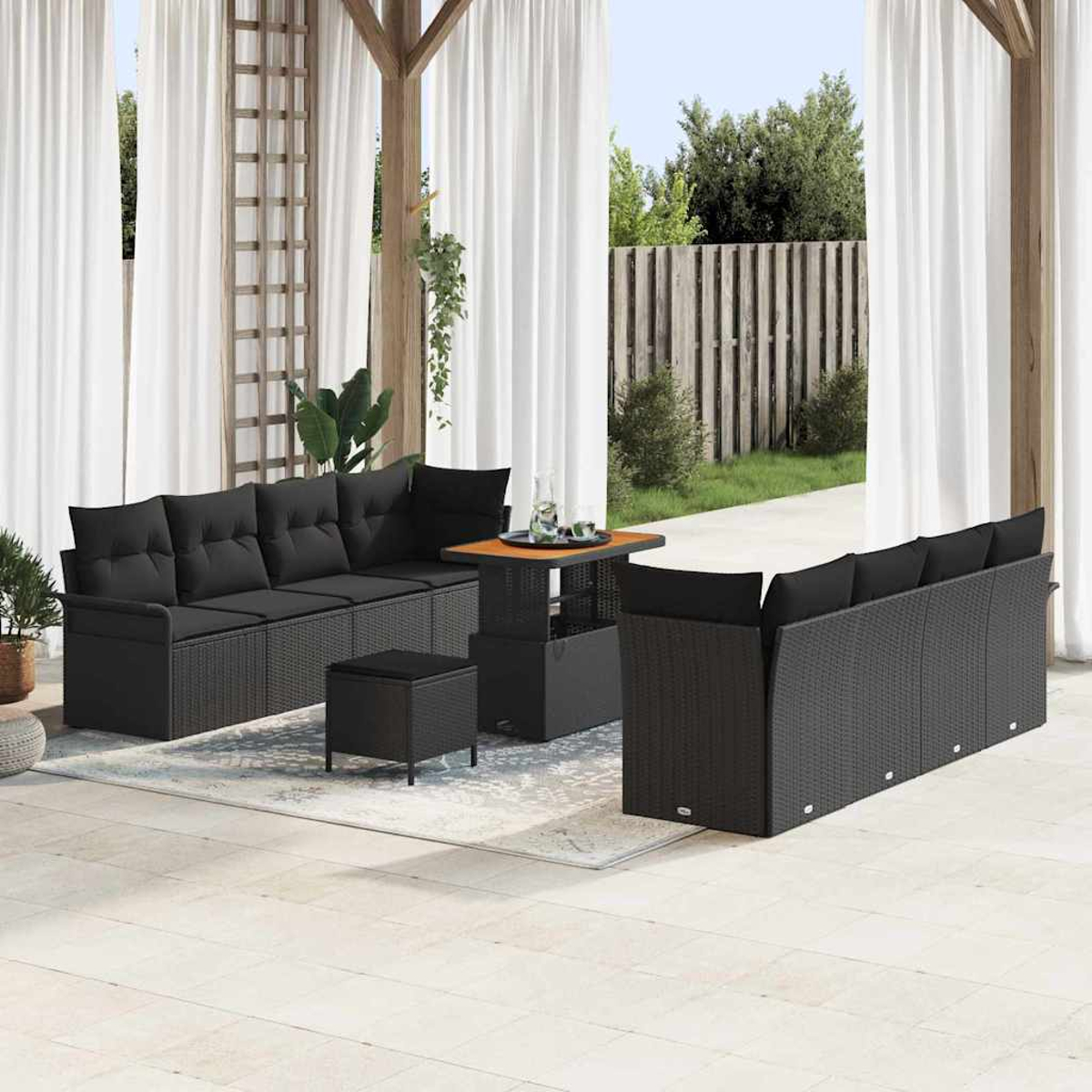 Garten-Terrassenset mit schwarzen Korbmöbeln, Sofa, Stühlen, Tisch und Ottomane. Weiße Vorhänge im Hintergrund.