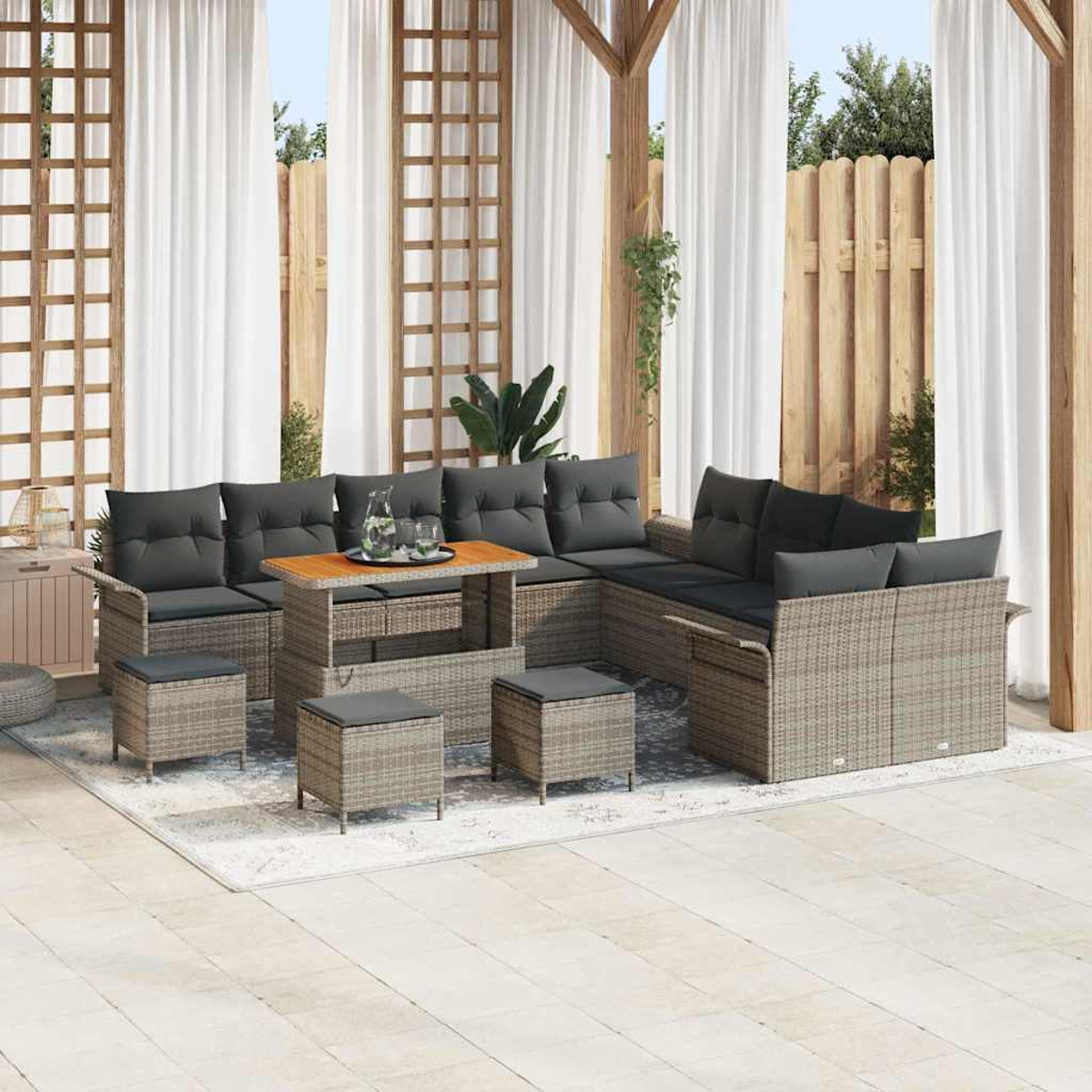 Garten-Sitzgruppe auf einer Terrasse. Beinhaltet Ecksofa, Tisch und Ottomanen. Weiße Vorhänge und Holzzaun im Hintergrund.