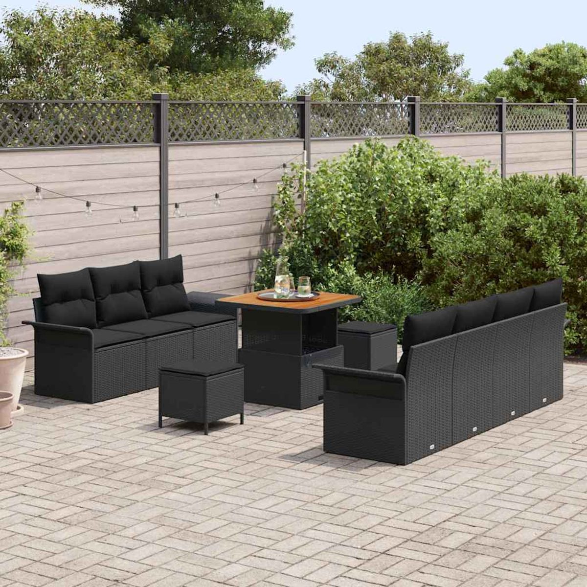 Gartenmöbel-Set: Zwei Sofas, zwei Hocker, ein Tisch und zwei Stühle stehen auf einer Backstein-Terrasse mit Zaun.