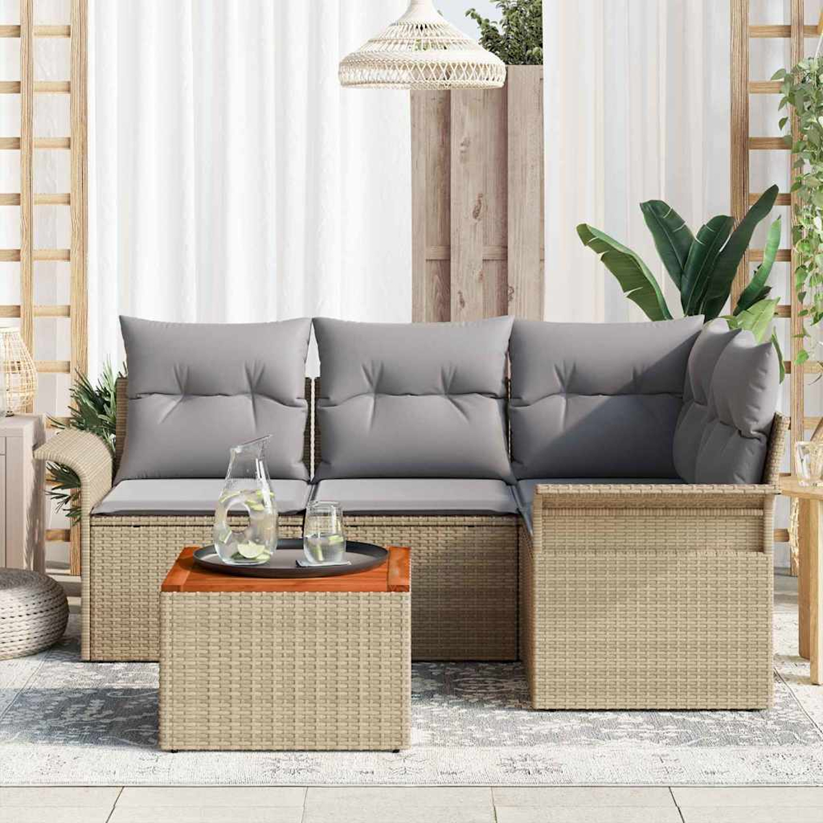 Gartenmöbel-Set aus Korbgeflecht mit grauen Kissen, einem Holztisch und einem Glaskrug auf einem Outdoor-Teppich.
