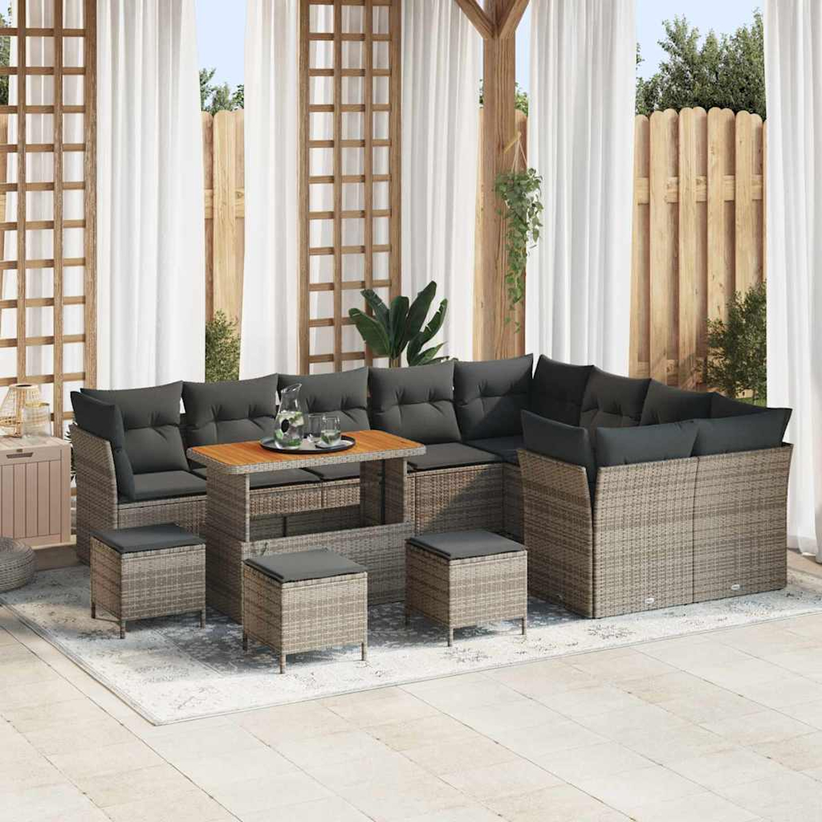 Gartenmöbel-Set aus Korbgeflecht mit grauen Kissen und Holztisch. Enthält Sofas, Ottomanen und einen Teppich. Weiße Vorhänge und Holzstruktur.