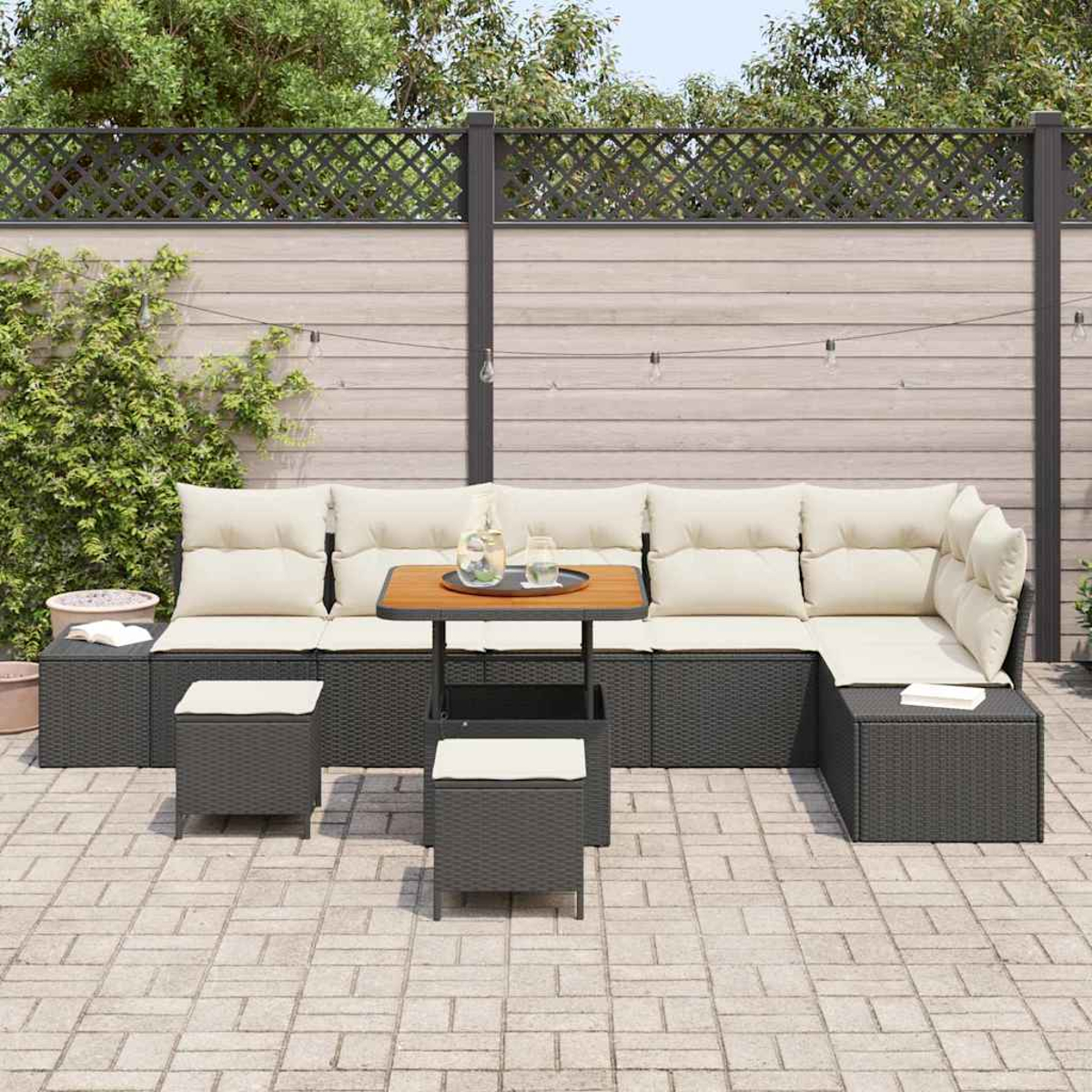 Outdoor-Terrassenset: graues Korbsessel-Ecksofa mit cremefarbenen Kissen, kleinem Tisch und zwei Ottomanen auf einer Ziegelterrasse, mit Zaun.