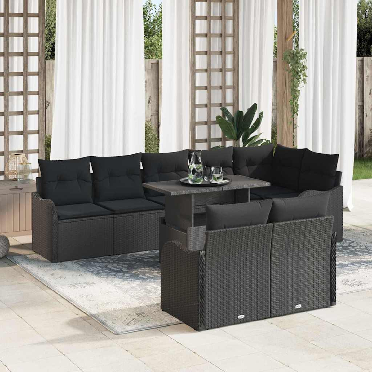 Terrassenset im Freien mit schwarzen Kissen. Tisch mit Getränken, weiße Vorhänge und Holzstruktur im Hintergrund. Teppich auf dem Boden.