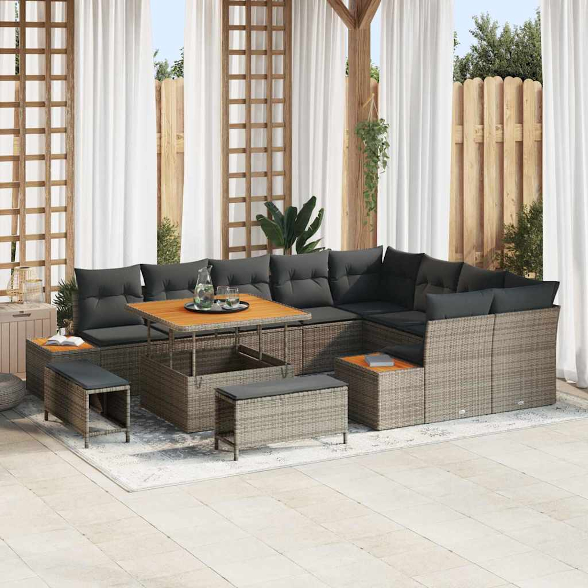 Gartensektionssofa mit grauen Kissen, Holztisch und Bänken. Weiße Vorhänge und Holzzaun im Hintergrund. Eine entspannende Szene im Freien.