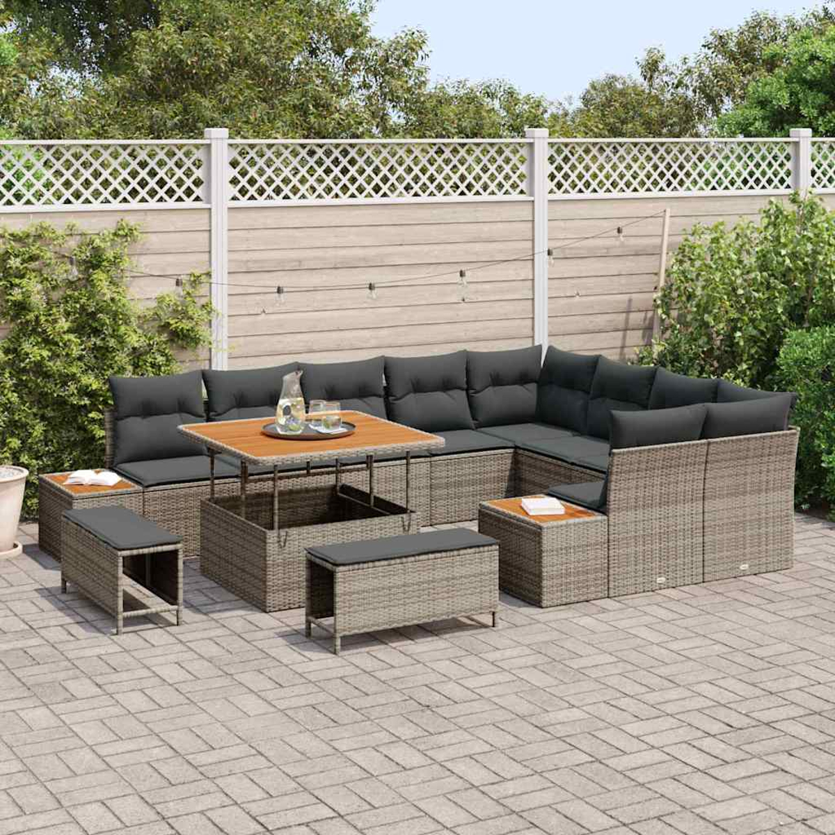 Gartenmöbel-Set mit grauen Kissen und einem Holztisch. Ein weißer Zaun und grüne Pflanzen im Hintergrund.