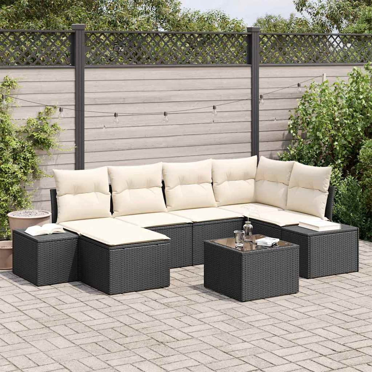 Gartenmöbel-Set mit cremefarbenen Kissen, Glastisch und grauem Korbmuster vor Holzzaun.