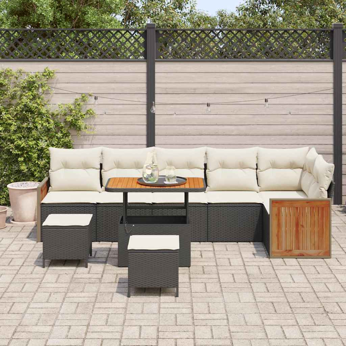 Garten-Terrassenset mit cremefarbenen Kissen, kleinem Holztisch und grauen Korbmöbeln. Im Hintergrund befinden sich ein Zaun und Grün.