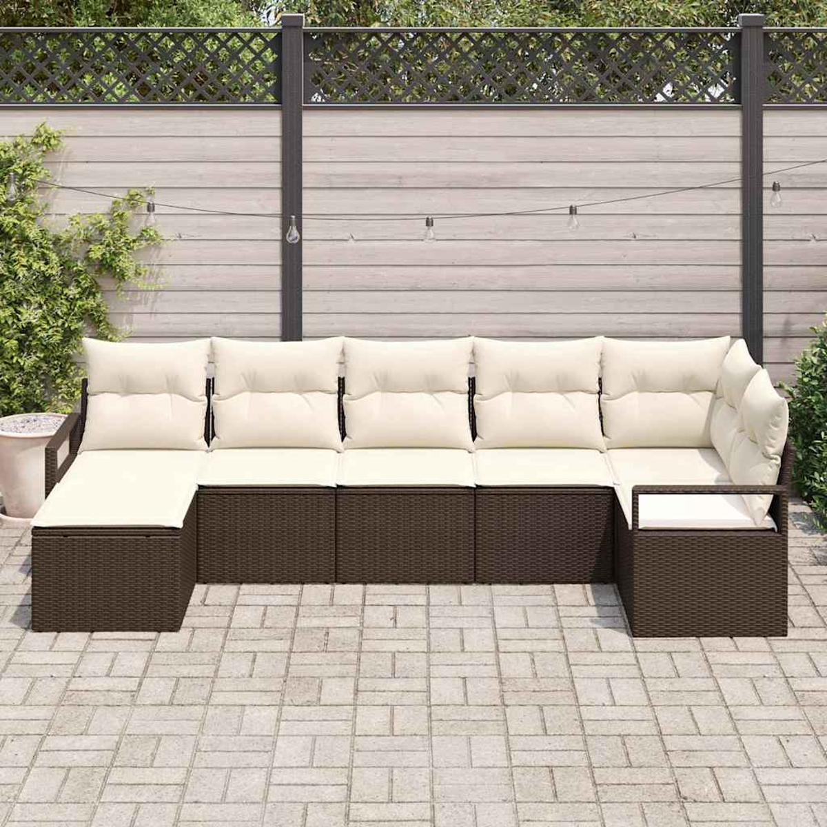 Braunes Outdoor-Ecksofa aus Korbgeflecht mit cremefarbenen Kissen. Es steht auf einer Ziegelterrasse, im Hintergrund ein Holzzaun.