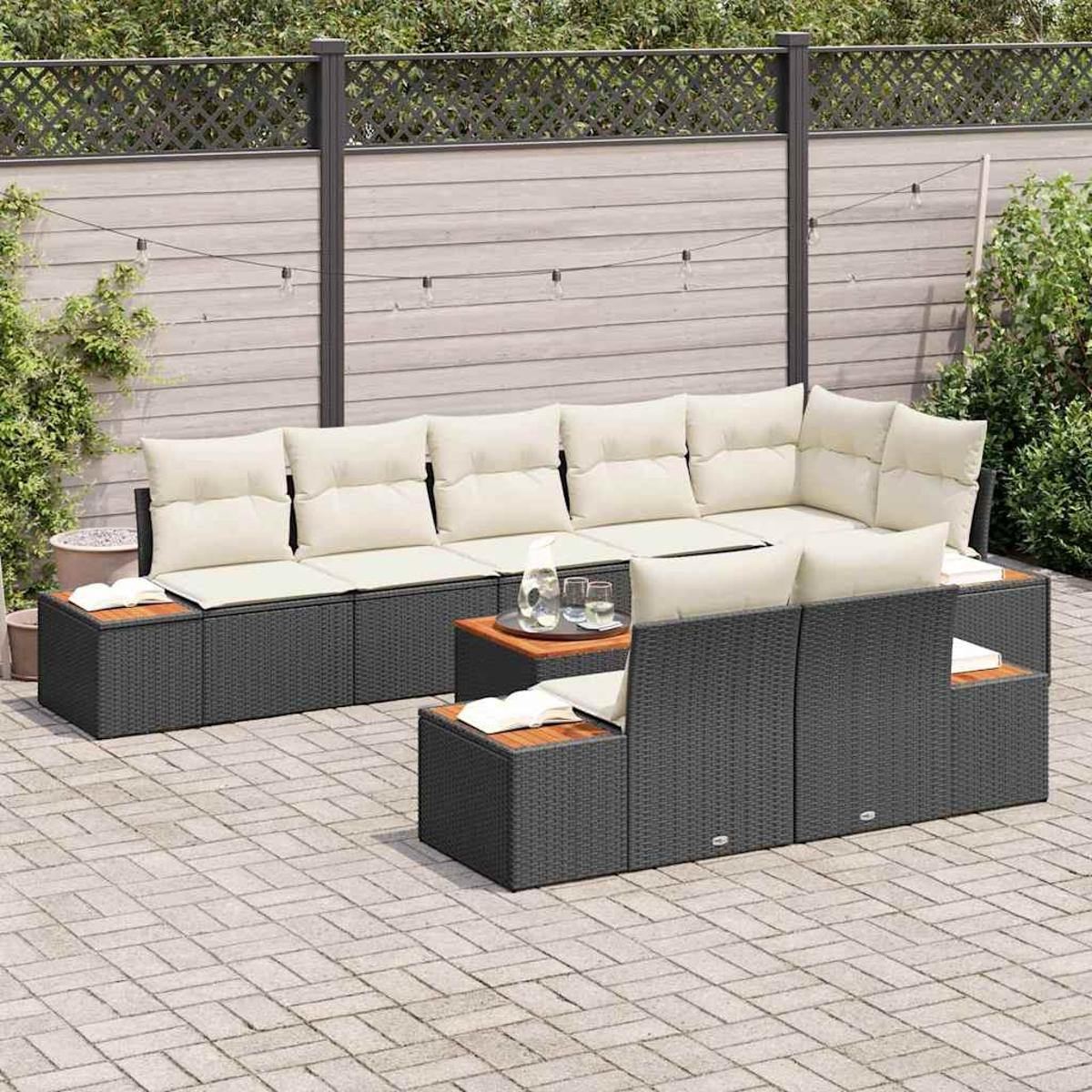 Outdoor-Terrassengarnitur: dunkelgraue Korbmöbel mit cremefarbenen Kissen, Holztischen und einer grauen Backstein-Terrasse. Im Hintergrund ein Holzzaun.