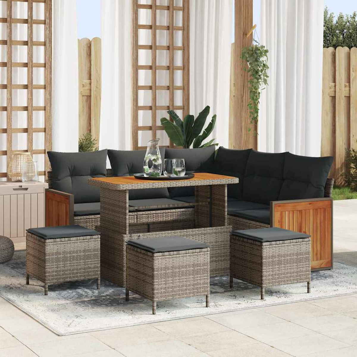 Garten-Terrassenset mit Rattanmöbeln, dunklen Kissen und einem Holztisch. Inklusive Teppich, Pflanzen und Vorhängen im Hintergrund.