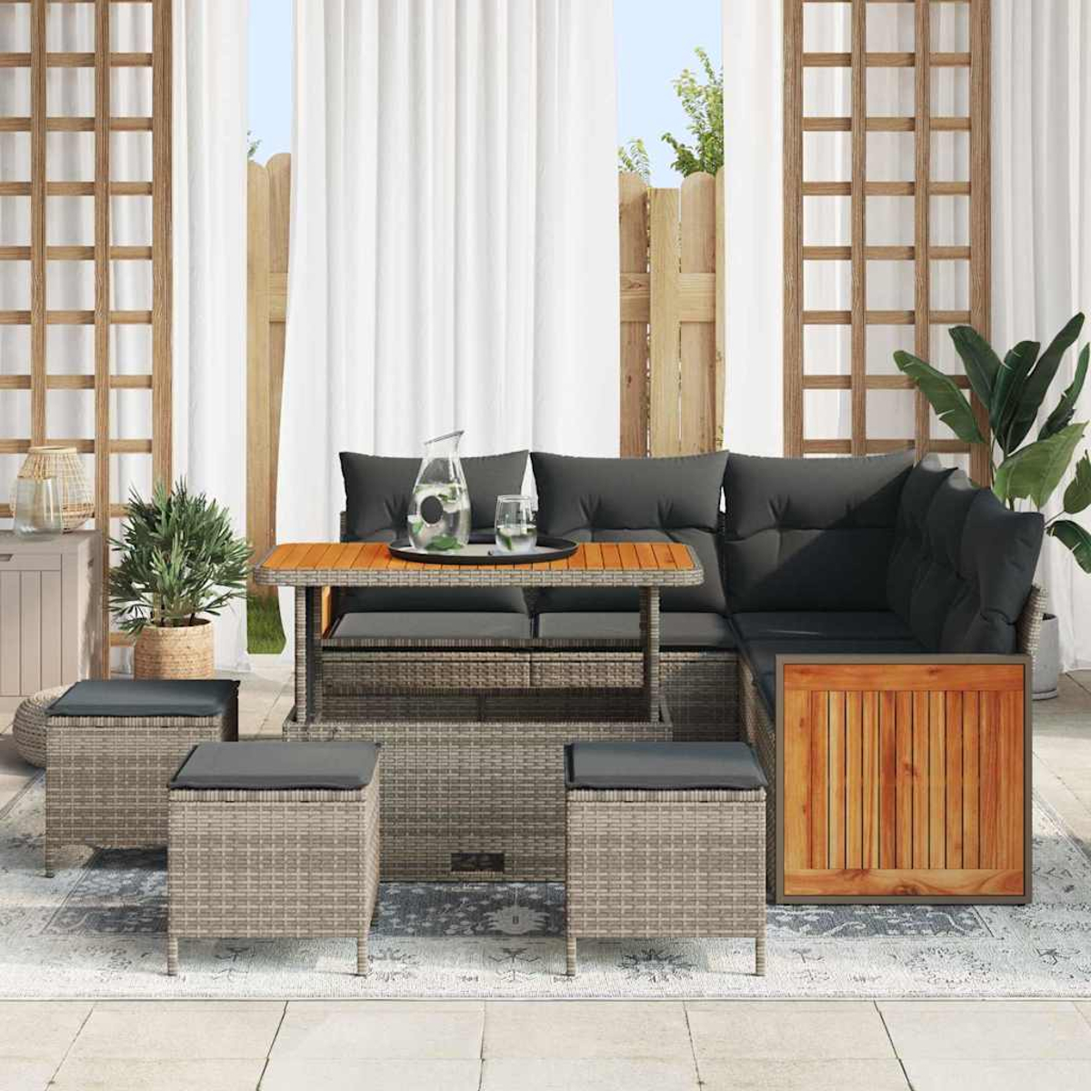 Outdoor-Sitzgruppe. Graues Korbmöbel-Ecksofa, Tisch mit Glas und vier Ottomanen auf einem gemusterten Teppich. Vorhänge und Pflanzen.