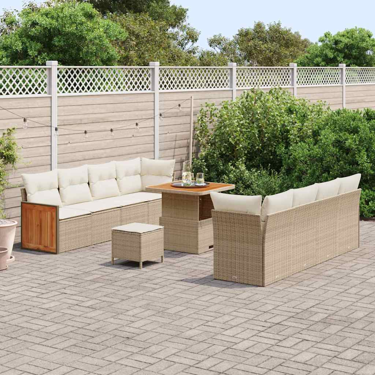 Conjunto de patio al aire libre con muebles de mimbre beige, una mesa con bebidas y una valla blanca en el jardín.