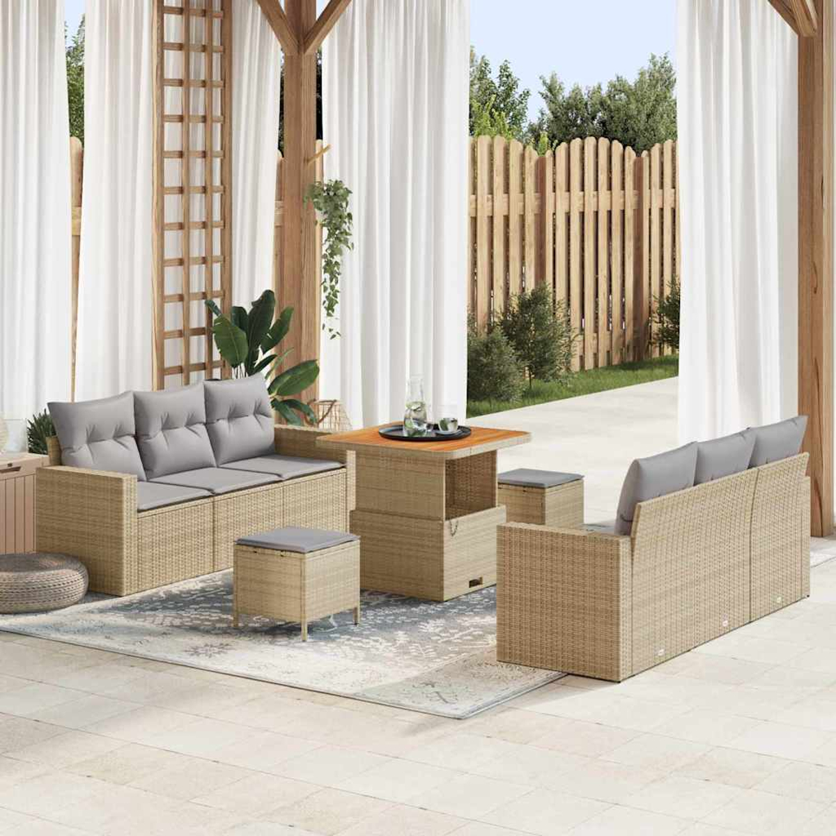 Gartenmöbel-Set aus Rattan auf einer Terrasse, darunter Sofas, ein Tisch und Ottomanen, mit weißen Vorhängen und einem Holzzaun im Hintergrund.
