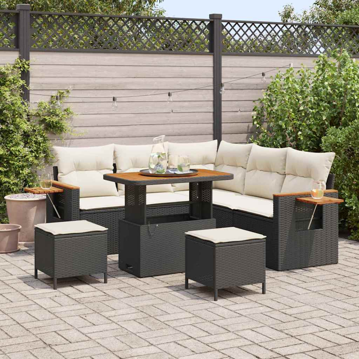 Terrassenset: dunkelgraues Korbmöbel, Holztisch und zwei Hocker mit beigen Kissen. Auf einer Ziegelterrasse.