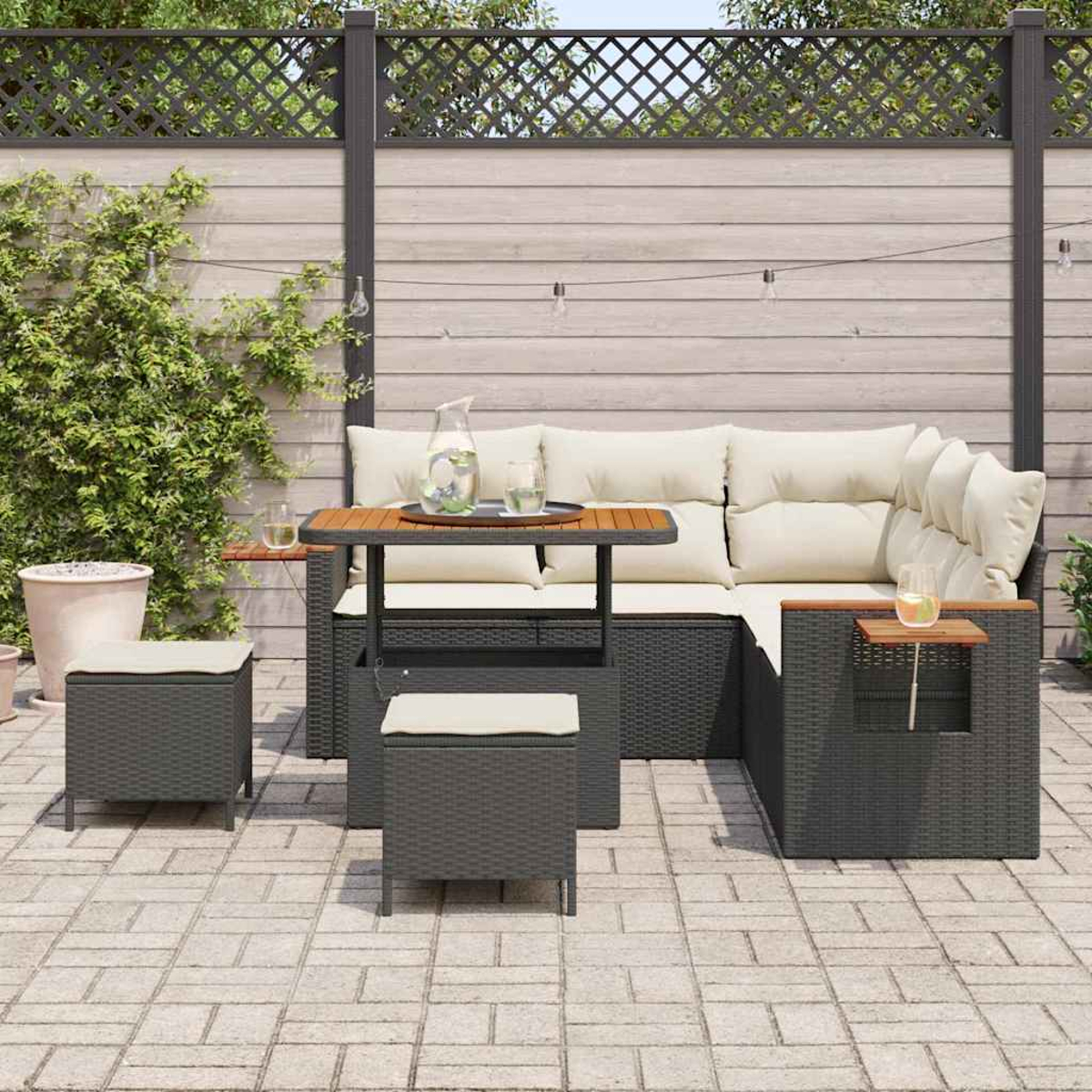 Garten-Sitzgruppe mit Kissen, Tisch und zwei Hockern. Auf einer Terrasse mit Holzzaun und Kletterpflanze.