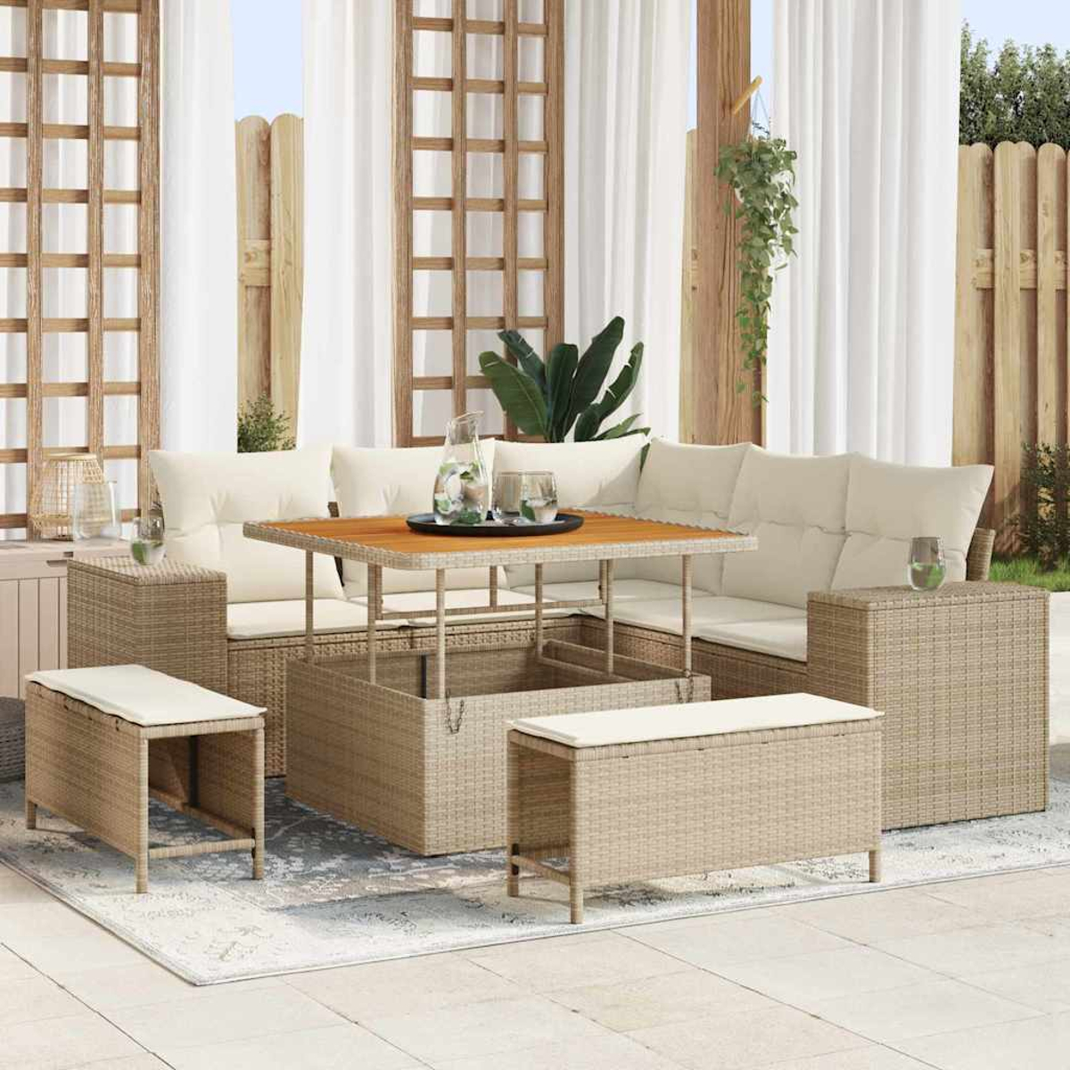Gartenmöbel-Set aus Rattan: Sofa, Tisch und Bänke mit cremefarbenen Kissen. Weiße Vorhänge und Holzgitter im Hintergrund.