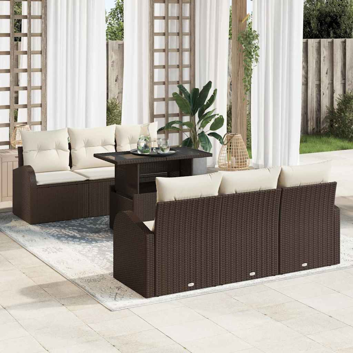 Rattan-Gartenset mit beigefarbenen Kissen. Ein Tisch und ein Teppich vervollständigen die Szene. Weiße Vorhänge und Pflanzen sind im Hintergrund.