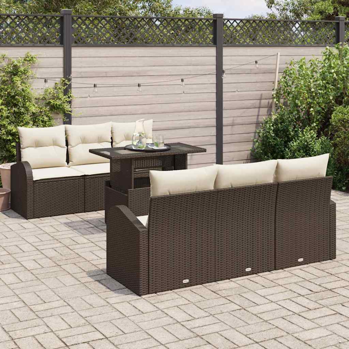 Gartenmöbel-Set: braune gewebte Sofas, beige Kissen, Glastisch und Hintergrundzaun mit Lichtern.