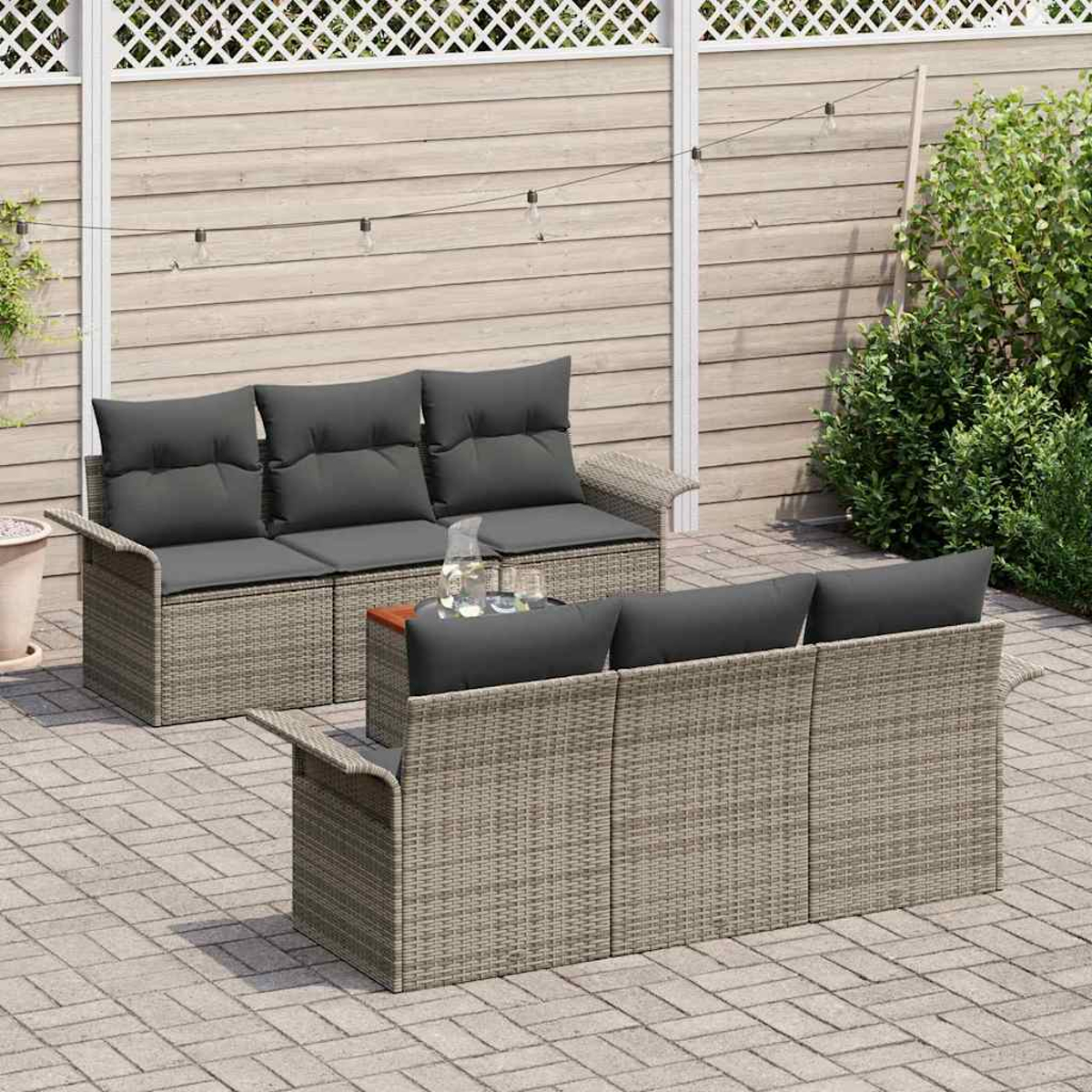 Gartenmöbel: zwei Korbs Sofas mit grauen Kissen, ein kleiner Tisch mit Gläsern, auf einer Terrasse. Holzzaun und Grün im Hintergrund.
