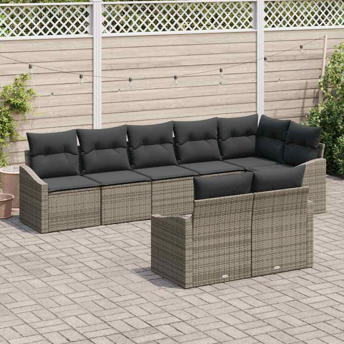 Garten-Terrassenset. Graues Korbmöbel-Sofa mit dunkelgrauen Kissen. Auf einer Backstein-Terrasse, mit Holzzaun im Hintergrund.