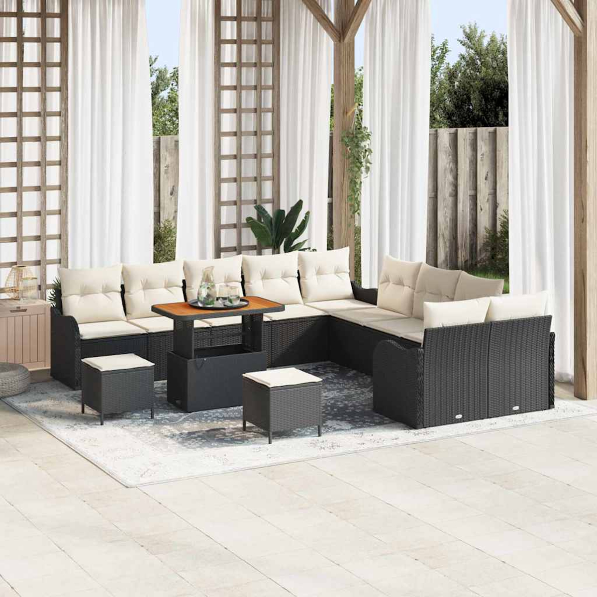 Outdoor-Sitzbereich mit schwarzen Korbmöbeln, cremefarbenen Kissen und einem Holztisch. Weiße Vorhänge und ein heller Teppich.