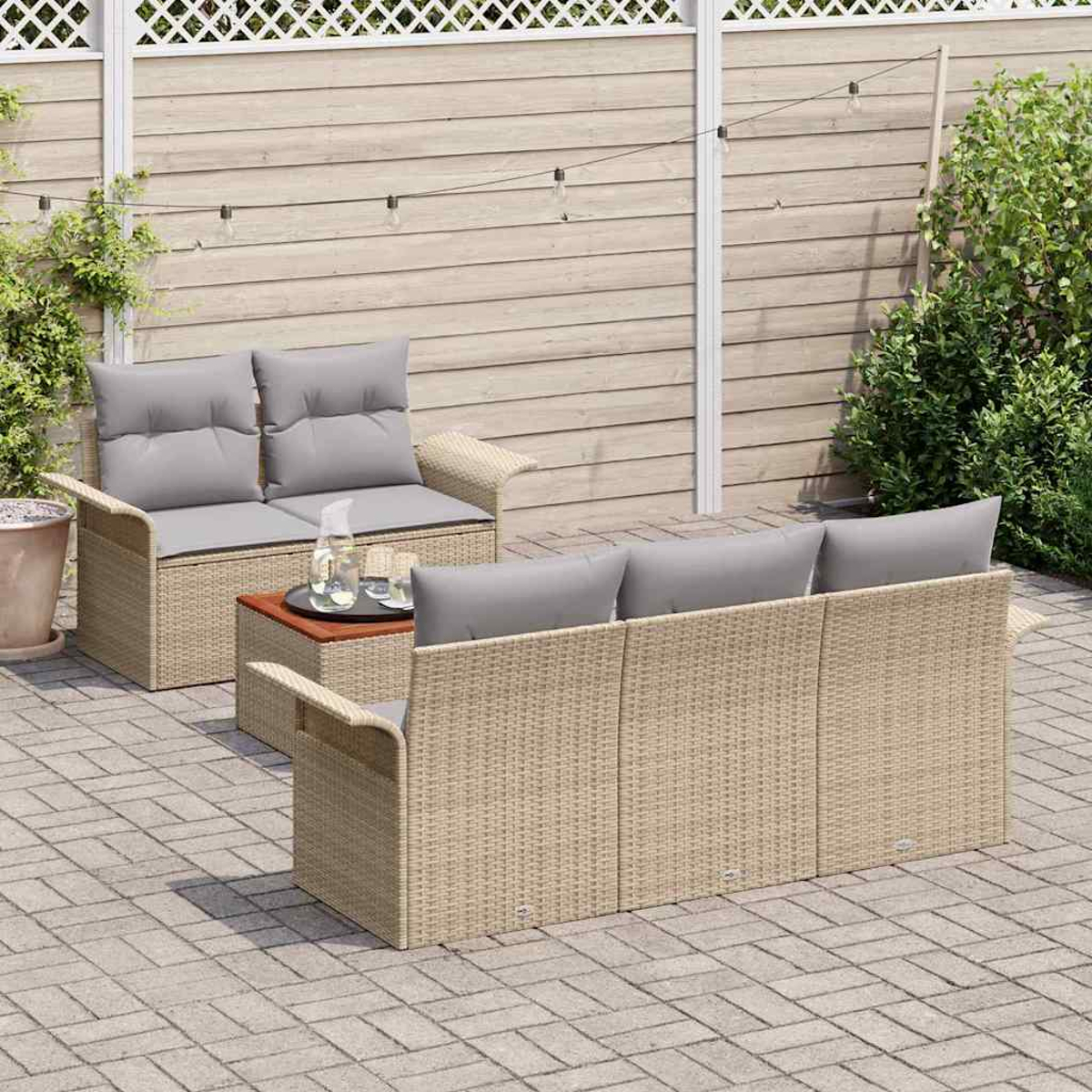 Szene im Freien mit Rattanmöbeln: ein Zweisitzer-Sofa, ein Dreisitzer-Sofa und ein Tisch. Graue Kissen. Holzzaun und Ziegelterrasse.