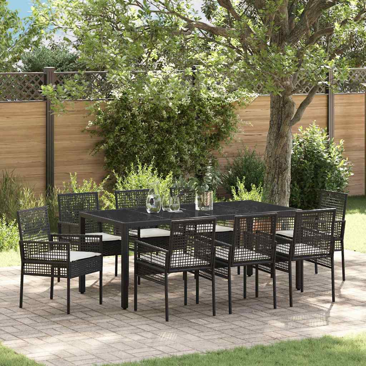 Essgruppe im Freien mit schwarzem Tisch und Stühlen. Die Terrasse hat Ziegelpflaster. Im Hintergrund befinden sich ein Holzzaun und Grün.