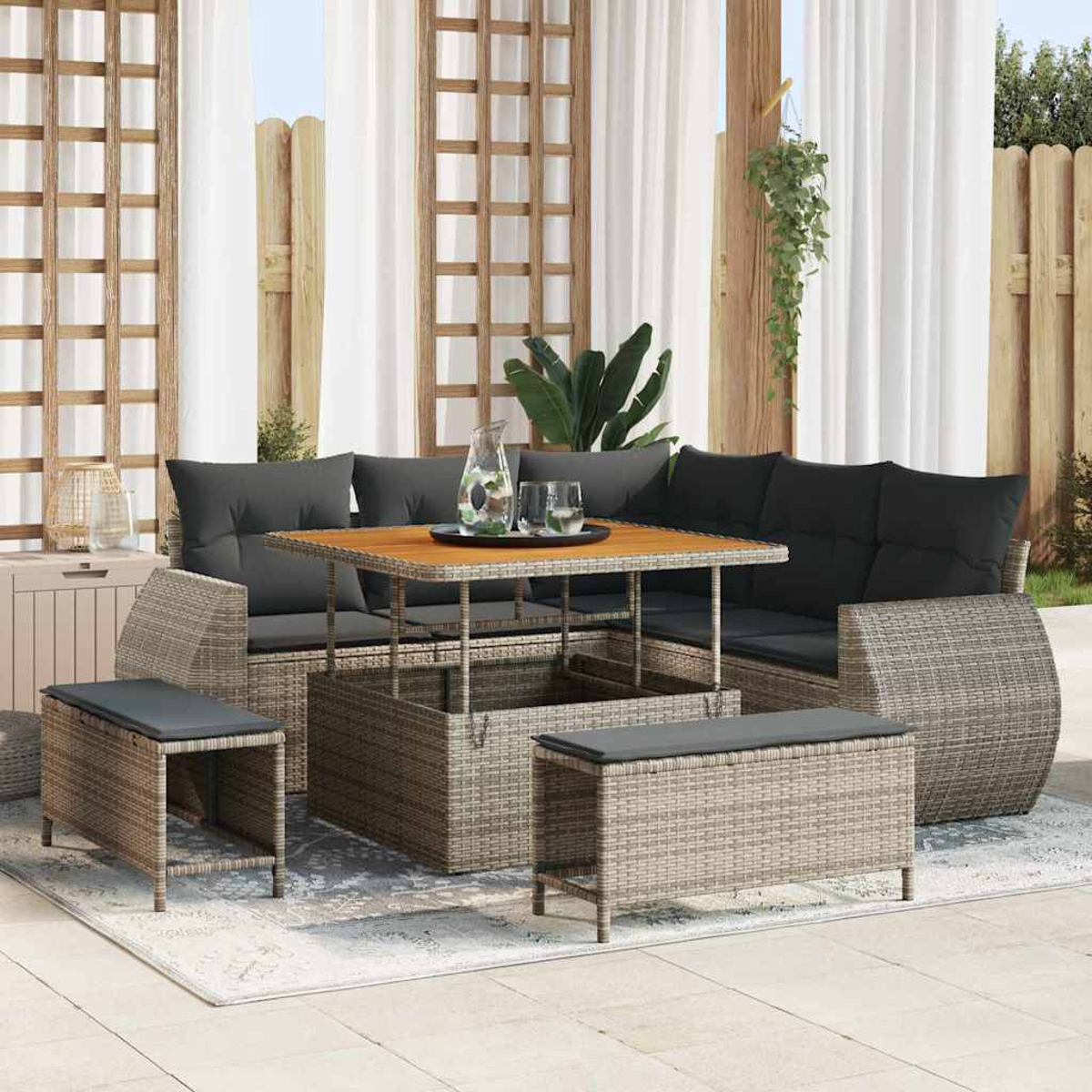 Outdoor-Sofa aus Korbgeflecht mit schwarzen Kissen, einem Holztisch und zwei Aufbewahrungshockern auf einem gemusterten Teppich.
