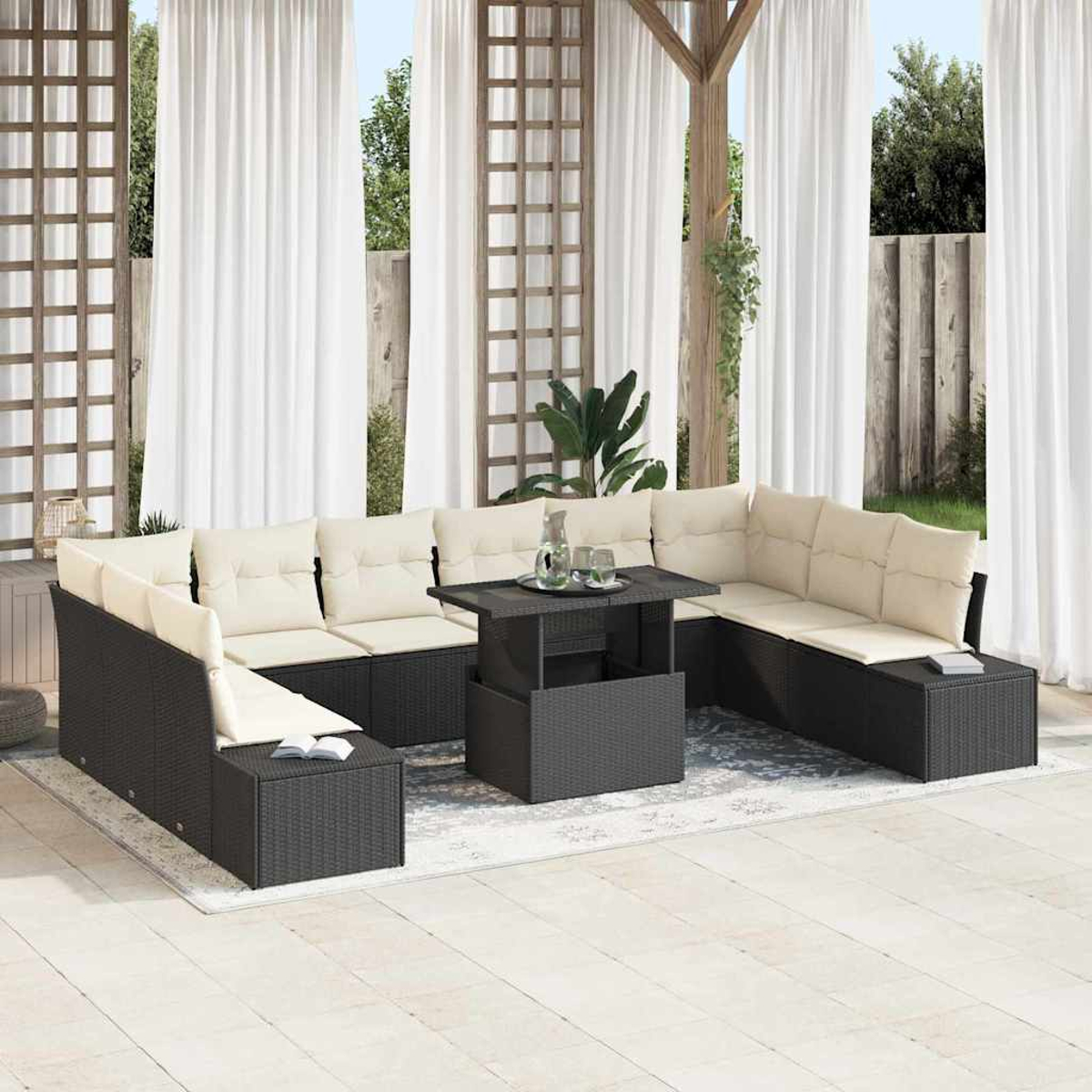 Outdoor-Sitzbereich mit schwarzem Rattan-Ecksofa, beigen Kissen und einem Tisch mit Hubfunktion. Weiße Vorhänge und Grün im Hintergrund.