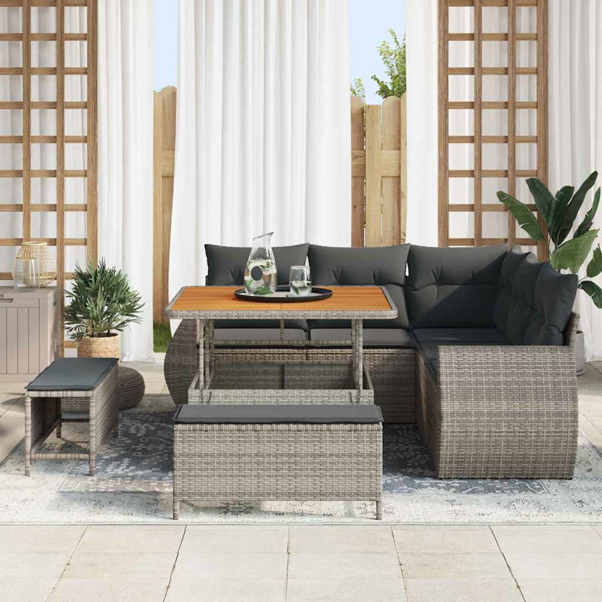 Outdoor-Sitzgruppe mit grauen Kissen, einem Holztisch und einer Bank. Im Hintergrund weiße Vorhänge und ein Holzzaun.