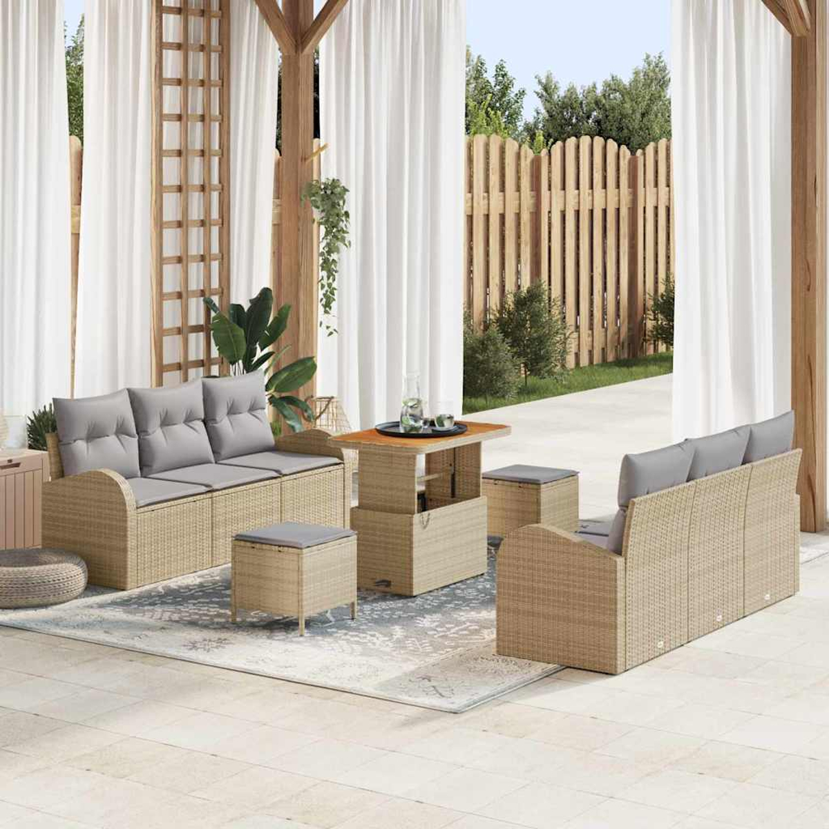 Terrassenset mit beigen Korbmöbeln, grauen Kissen und einem Holztisch. Weiße Vorhänge und ein Holzzaun sind im Hintergrund.