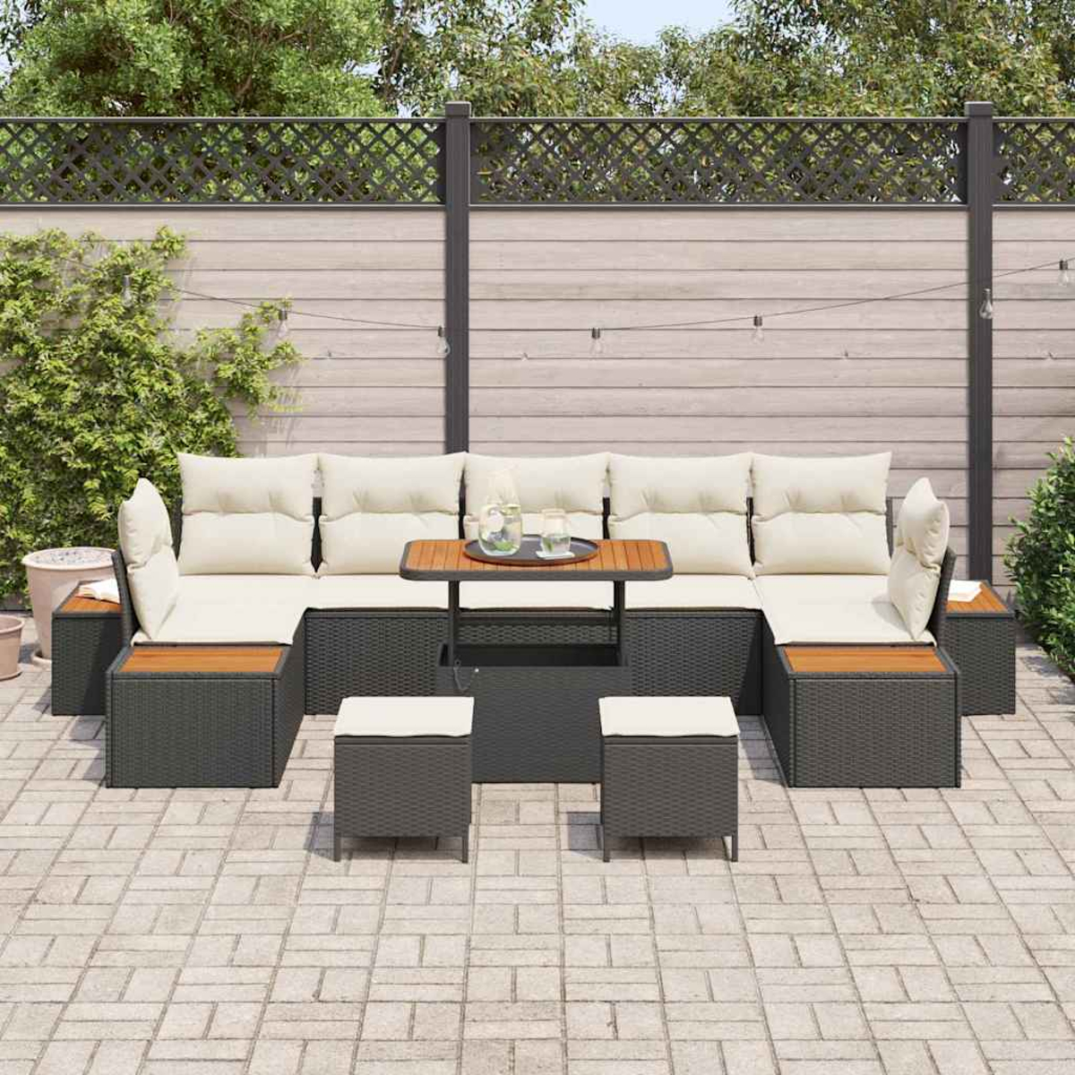 Outdoor-Ecksofa mit cremefarbenen Kissen, Holztisch und zwei Hockern auf einer Terrasse. Im Hintergrund ein Zaun und Pflanzen.