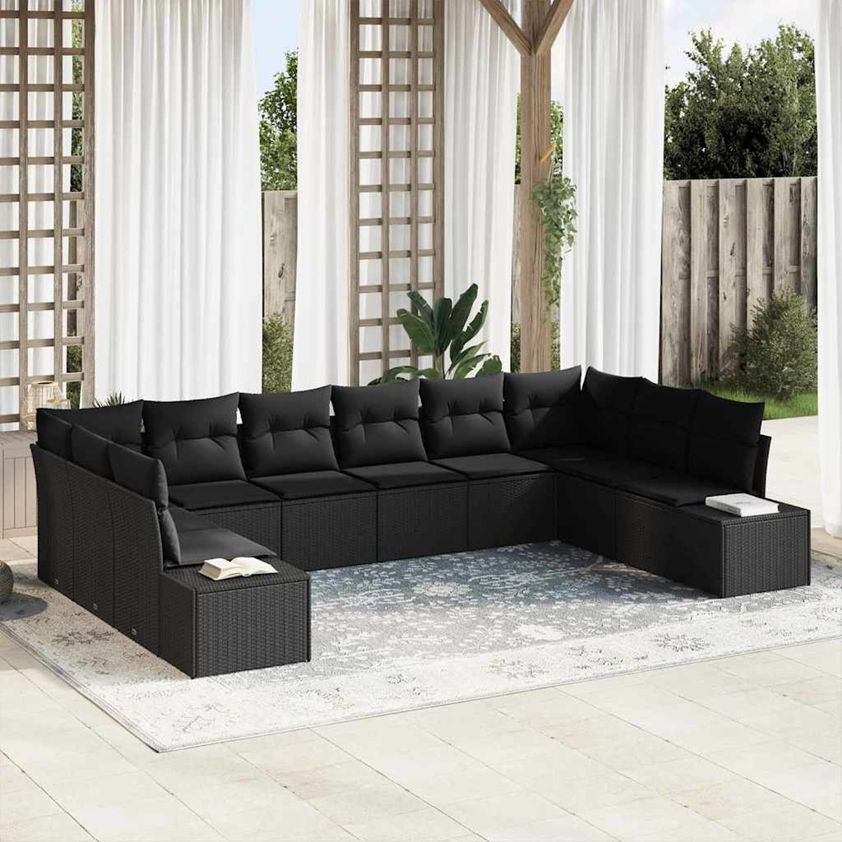 Schwarzes Outdoor-Ecksofa mit Kissen auf einem gemusterten Teppich. Weiße Vorhänge und Holzgitter im Hintergrund. Ein Buch liegt auf dem Sofa.