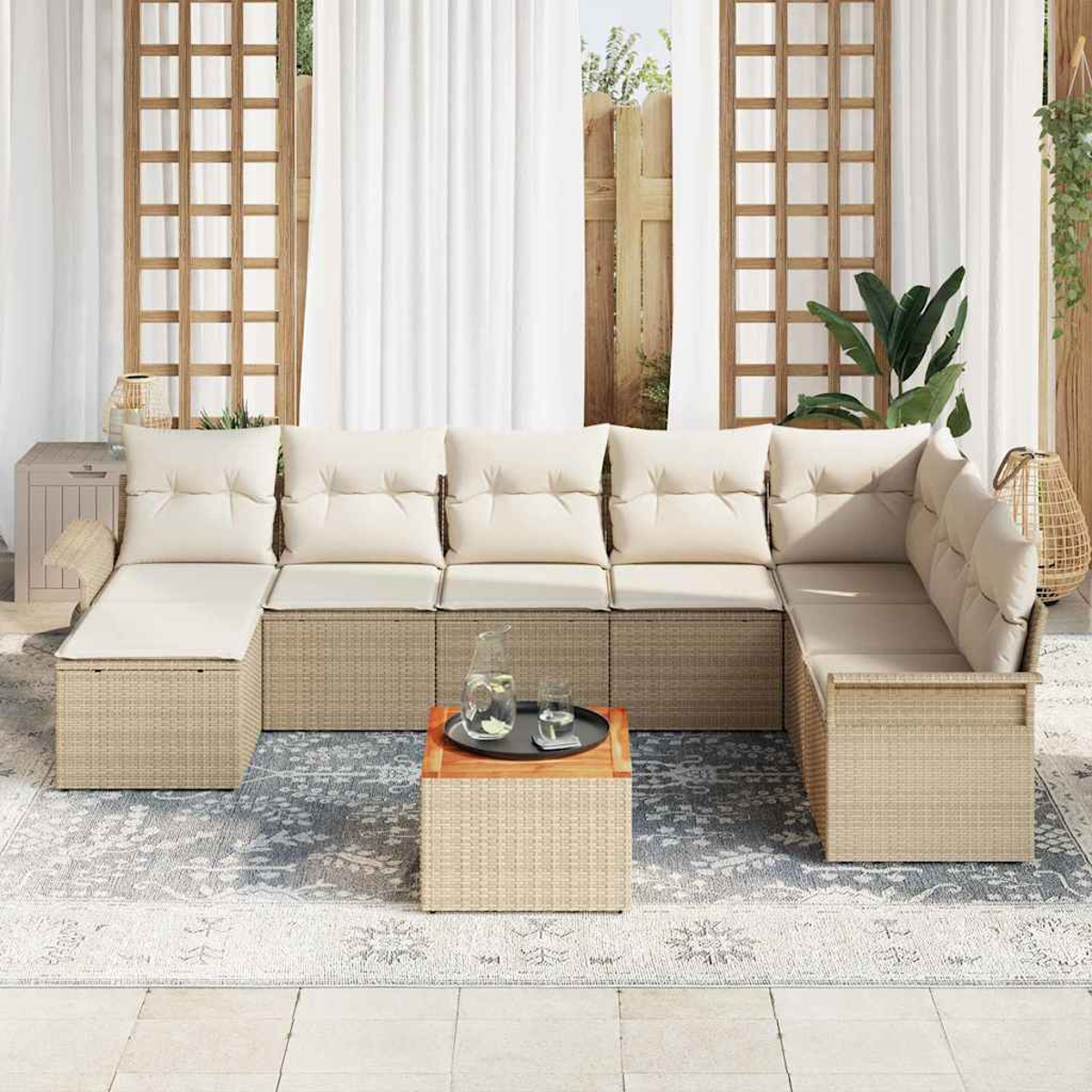 Outdoor-Ecksofa aus Korbgeflecht mit cremefarbenen Kissen, einem Holztisch und einem Teppich auf einer Terrasse. Dahinter weiße Vorhänge und ein Holzzaun.
