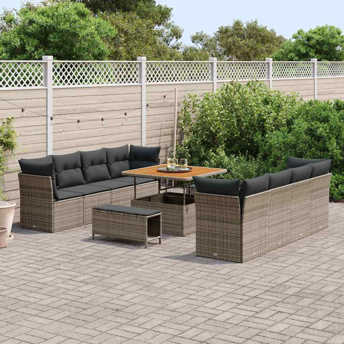 Garten-Terrassenset mit grauen Kissen. Enthält Sofa, Tisch und Bank. Auf einer Ziegelterrasse mit Zaun und Grün im Hintergrund.