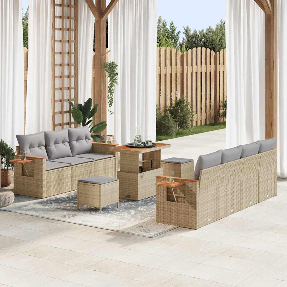 Garten-Terrassenset mit Korbmöbeln, grauen Kissen, einem Tisch und Hockern. Weiße Vorhänge, Holzzaun und Grün im Hintergrund.