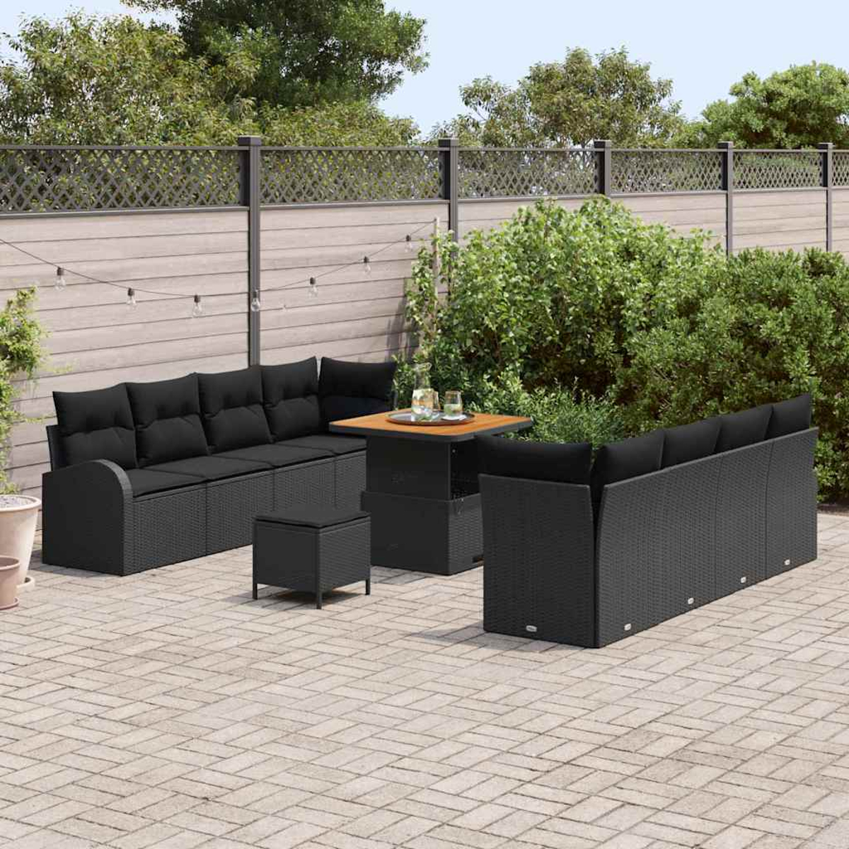 Terrassenset im Freien mit schwarzen Korbmöbeln, darunter Sofas, ein Tisch und ein Hocker, auf einer Backsteinterrasse, mit Holzzaun im Hintergrund.