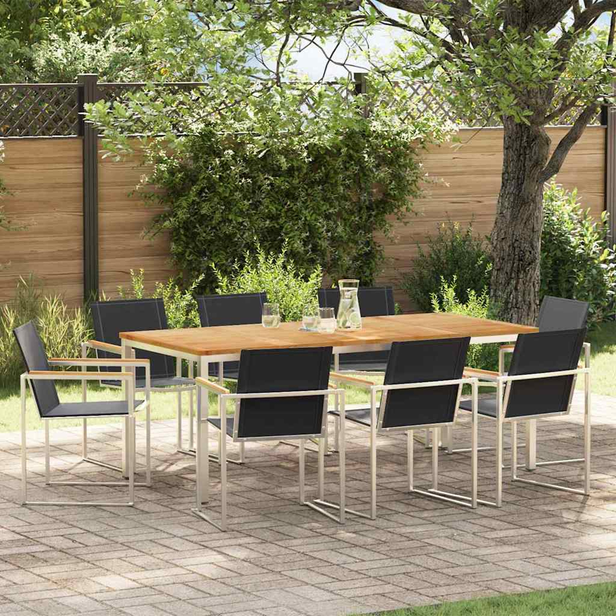 Juego de comedor al aire libre con mesa de madera y sillas negras. La escena incluye una valla de madera, árboles y un patio de ladrillos.