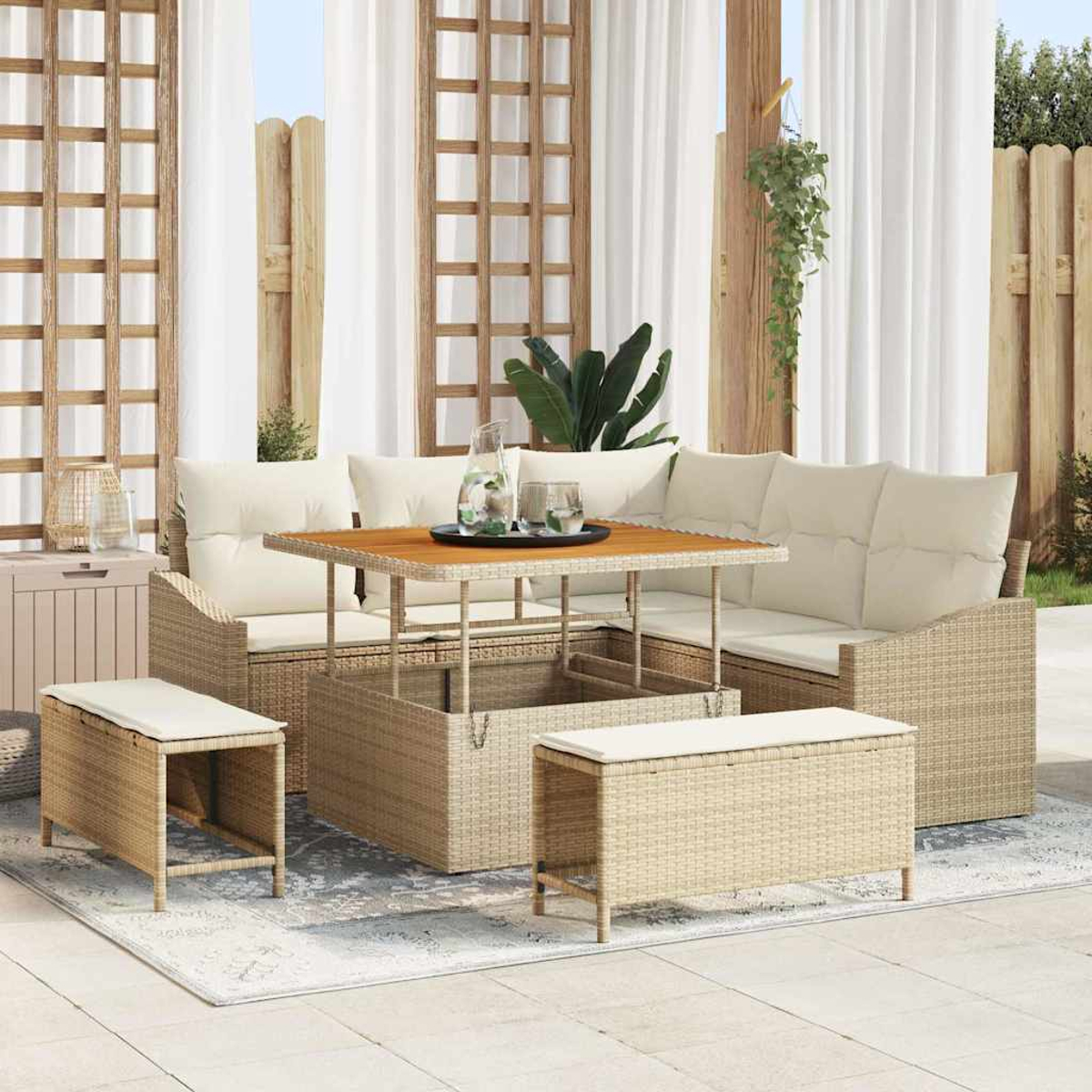 Gartenmöbel-Set aus Korbgeflecht. Enthält Sofa, Tisch und Bänke mit cremefarbenen Kissen. Weiße Vorhänge, Holzgitter und Pflanzen im Hintergrund.