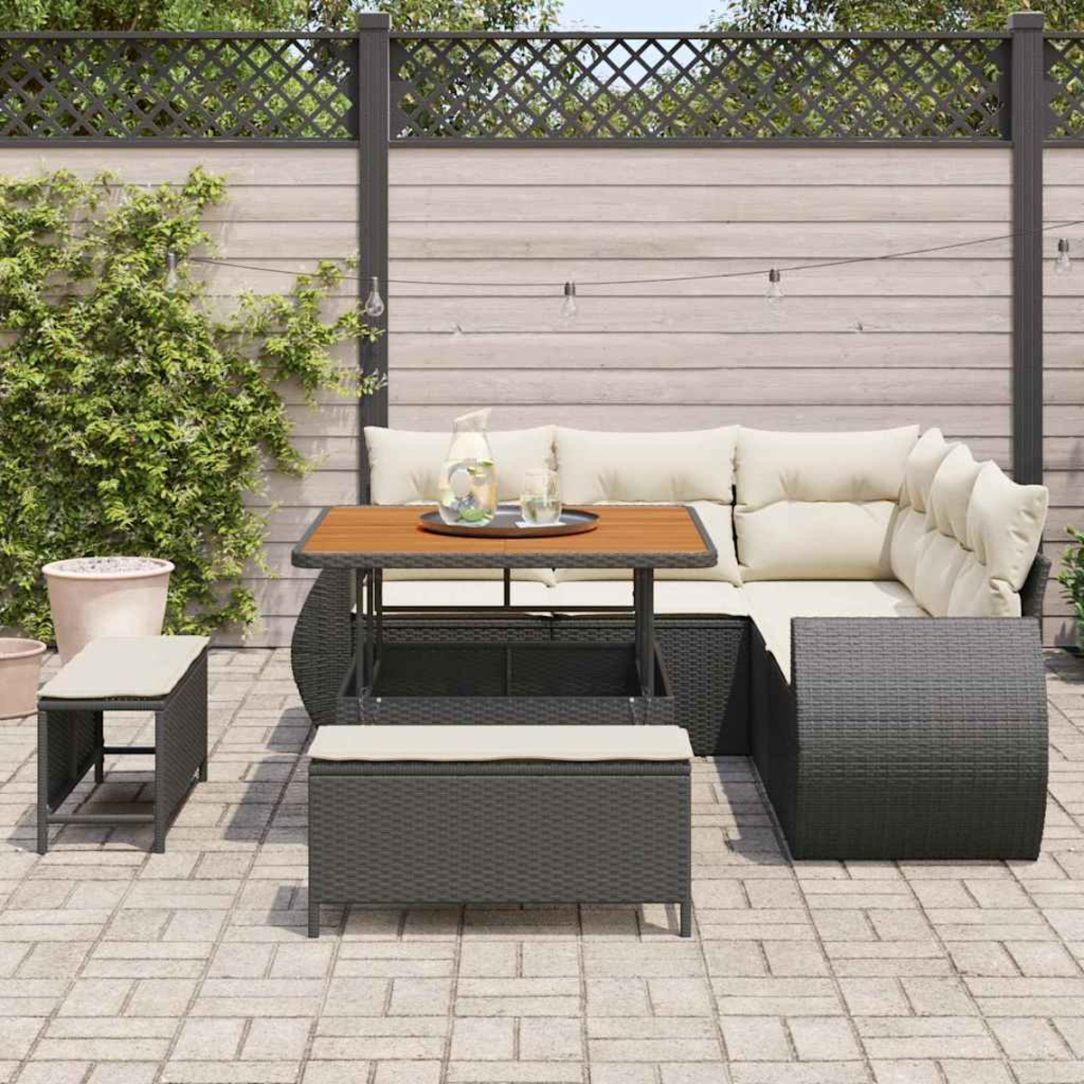 Eine Szene auf der Terrasse mit Korbmöbeln: ein Ecksofa, ein Tisch mit Tablett und zwei Bänke. Im Hintergrund ein Holzzaun.