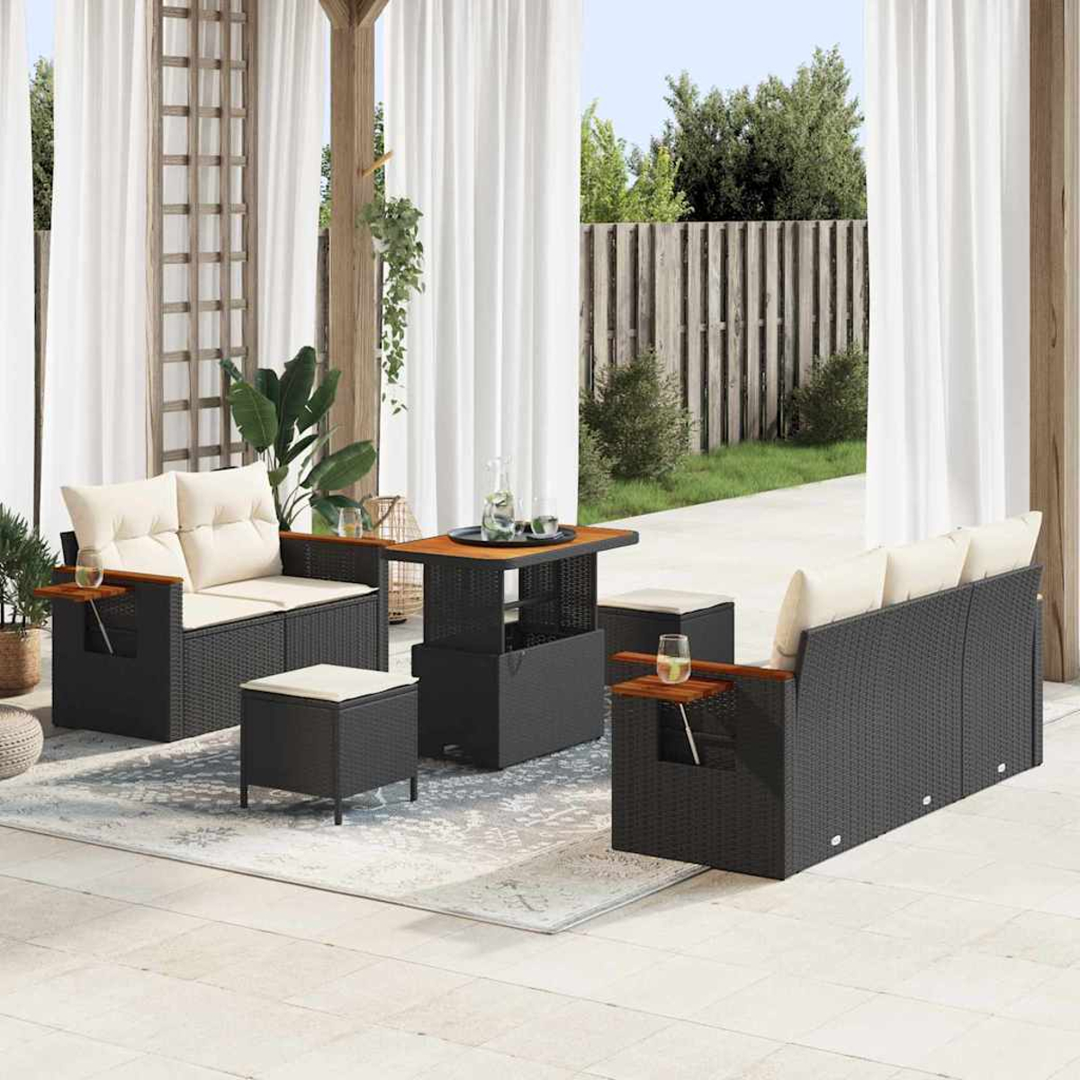 Set da patio esterno con divano, sedie, tavolo e pouf. Cuscini color crema, braccioli in legno e telai intrecciati neri. Tende bianche sullo sfondo.