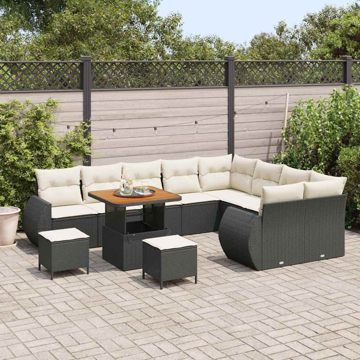 Outdoor-Ecksofa mit beigen Kissen, kleinen Tischen und Hockern auf einer Steinterrasse. Zaun und Grün im Hintergrund.