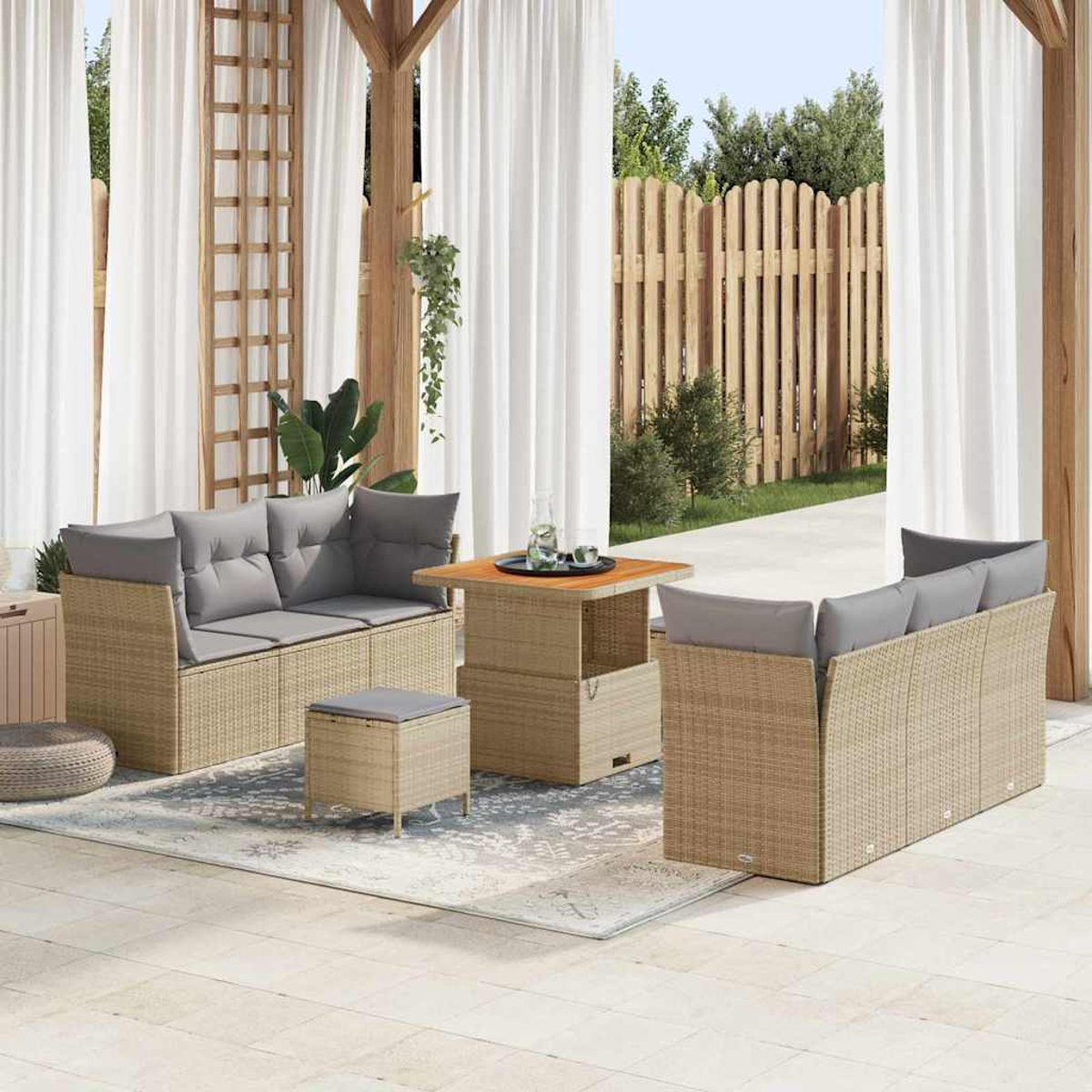 Juego de muebles de exterior con sofás beige tejidos, cojines grises y una mesa. Cortinas blancas, valla de madera y plantas forman el fondo.