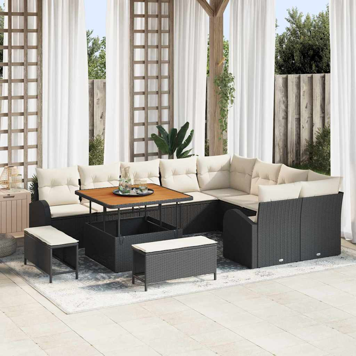 Garten-Terrassenset mit schwarzer Korbmöbel, beigefarbenen Kissen und einem Holztisch. Weiße Vorhänge und grüne Pflanzen im Hintergrund.