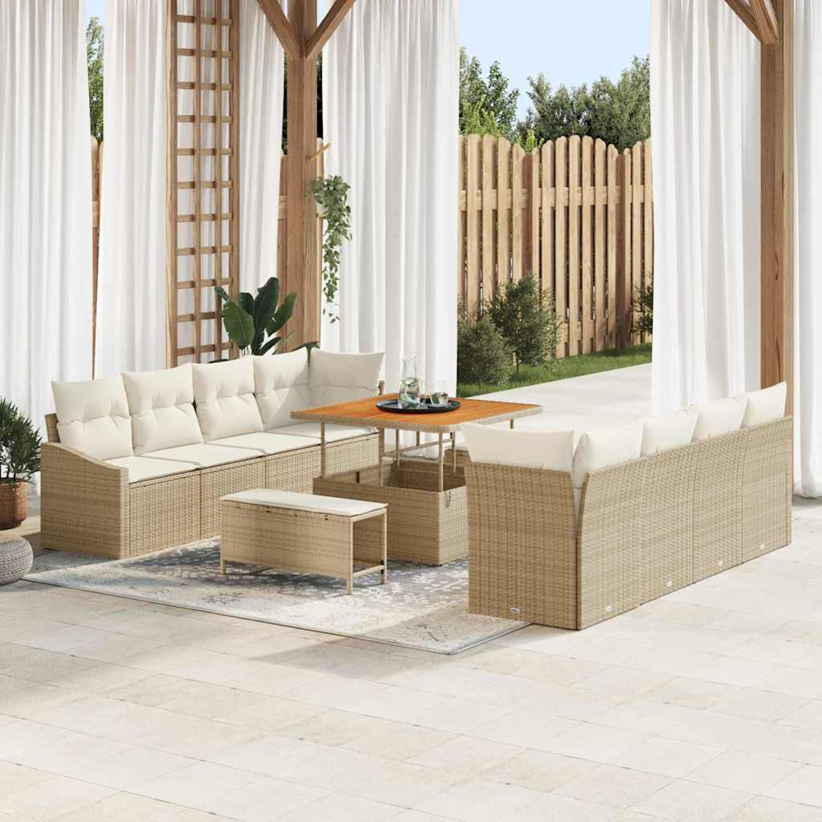Gartenmöbel-Set. Beige Rattan-Sofas mit weißen Kissen, Tisch und Bank. Weiße Vorhänge und Holzzaun im Hintergrund.